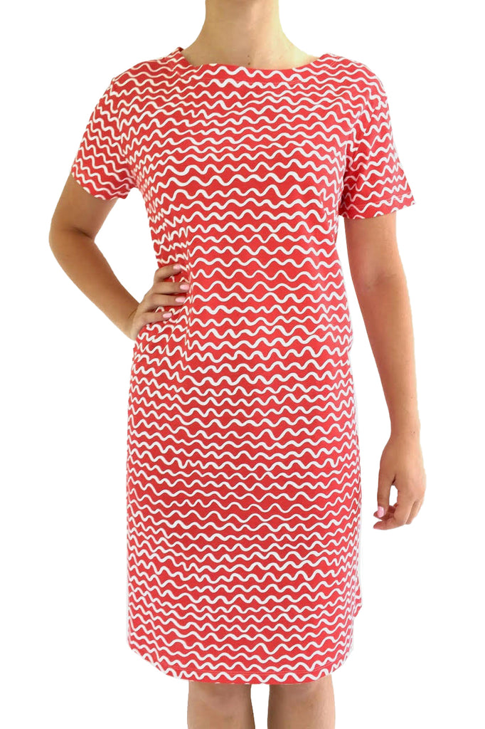 A person wearing a red dress with a white wavy pattern stands with one hand on their hip, showcasing the versatile Knit Dress Short Sleeve by See Design.