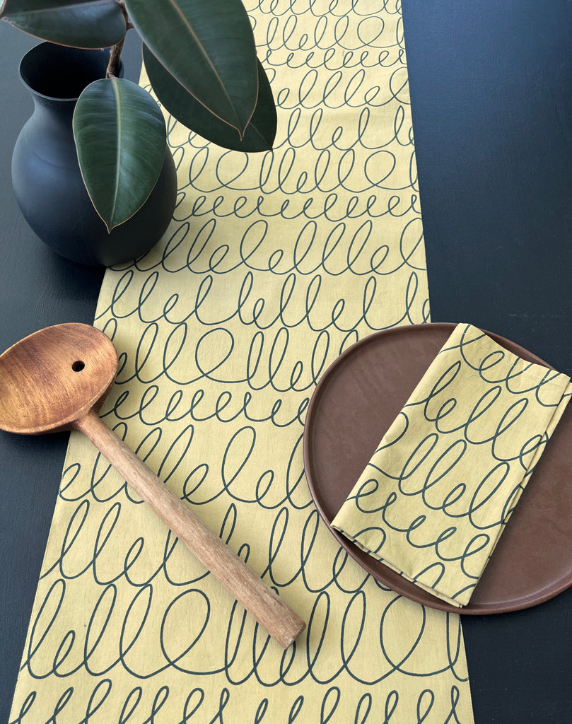 A yellow cotton See Design table runner with prints and colors.