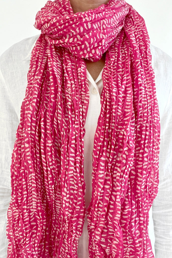 A woman wearing a See Design light pink cotton scarf with a crinkled texture.