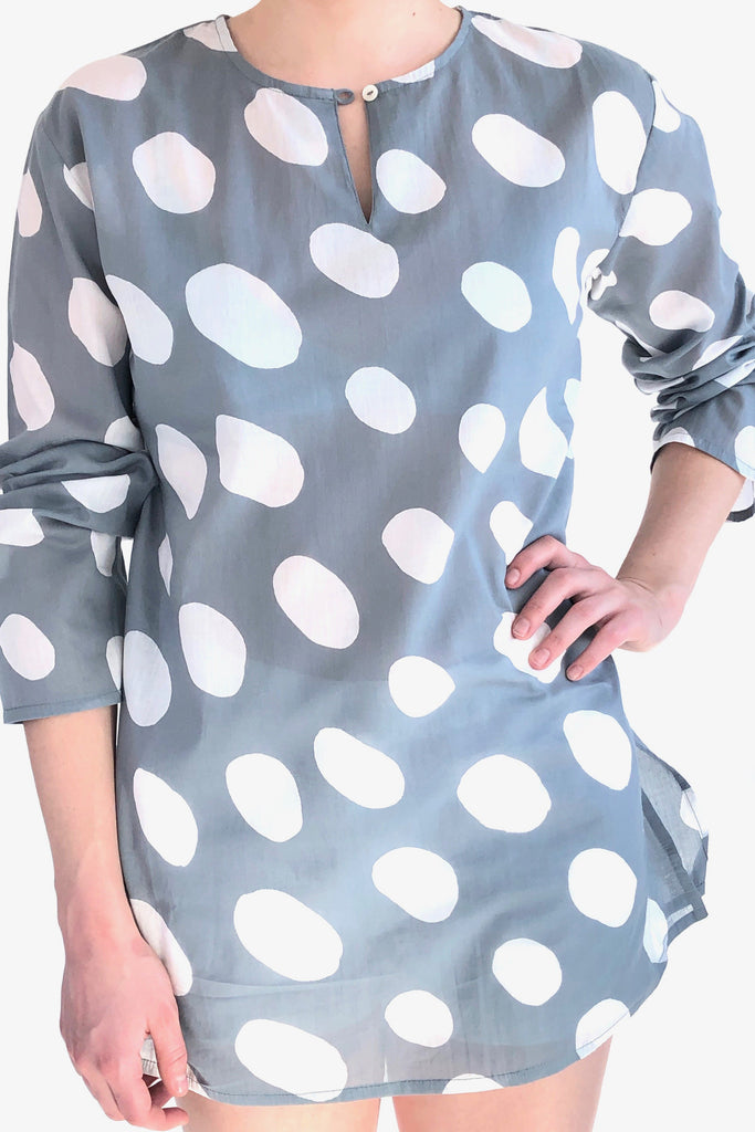A woman wearing a versatile, lightweight grey and white polka dot See Design tunic made of cotton voile.