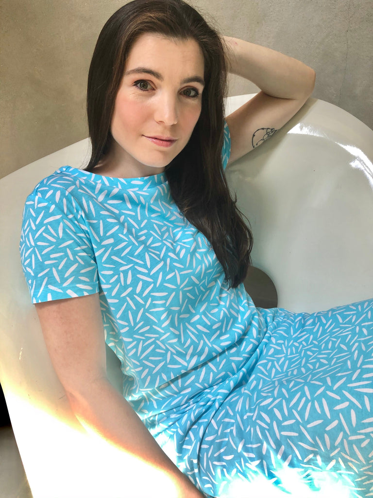 A comfortable woman in a versatile See Design blue knit dress short sleeve sitting on a chair.