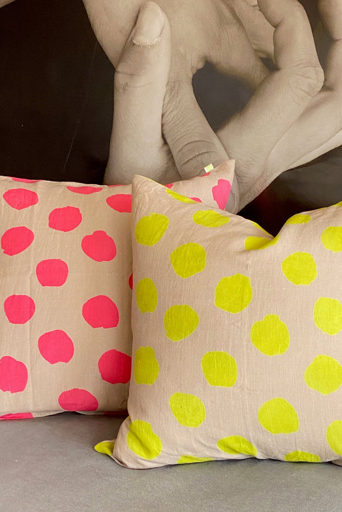 Two decorative See Design linen 26" Euro square pillow covers with pink and yellow polka dots in front of a grayscale photo of clasped hands.