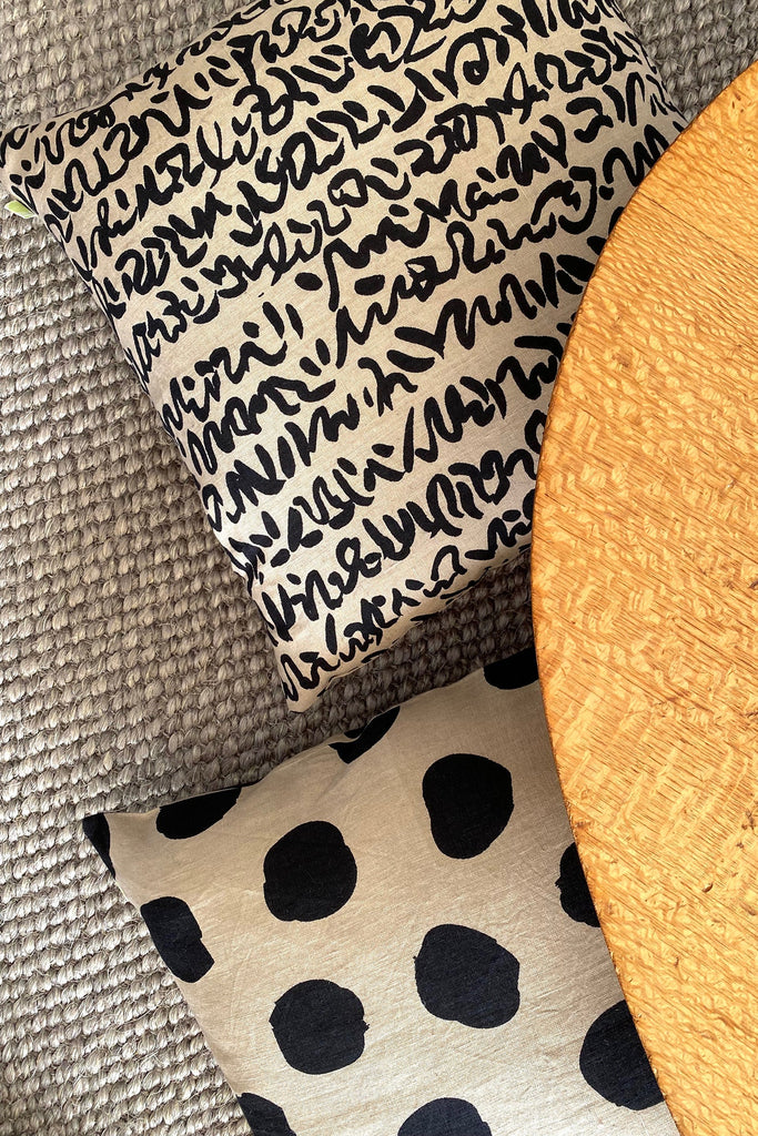 A See Design Linen 20" Pillow Cover covers a black and white polka dot pillow resting on a wooden table.