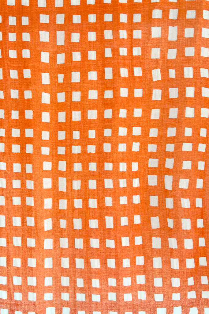 A close up of a bright orange and white checkered See Design Wool Scarf.