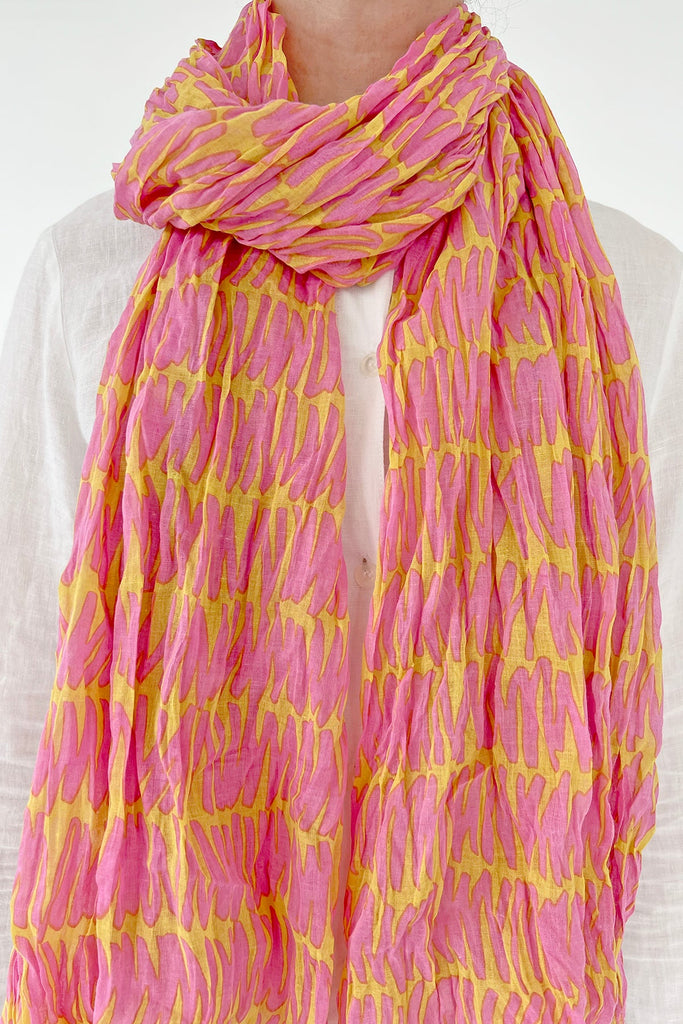 A woman wearing a lightweight and crinkled See Design cotton scarf in pink and yellow.