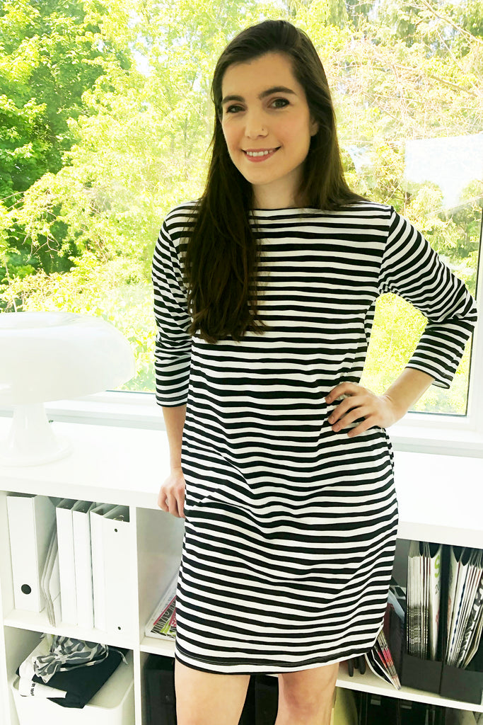 A versatile woman in a black and white striped See Design Knit Dress 3/4 Sleeve standing in front of a window.