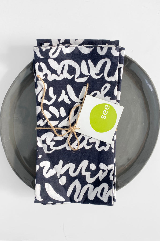 A set of vibrant See Design cotton napkins on a plate with a green tag.