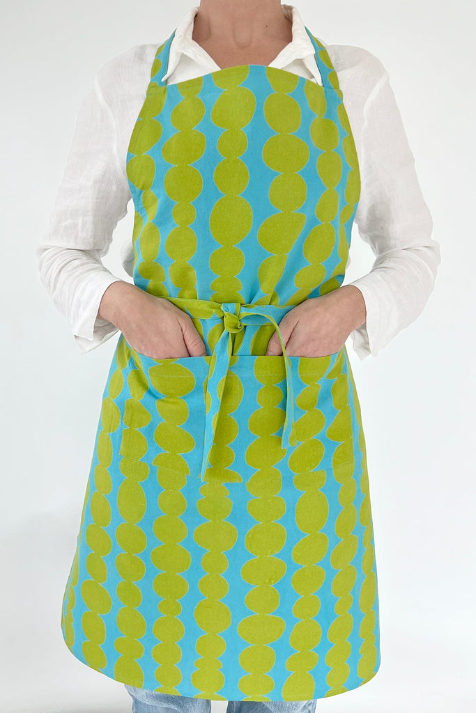 A woman wearing a See Design hand-painted blue and green apron.