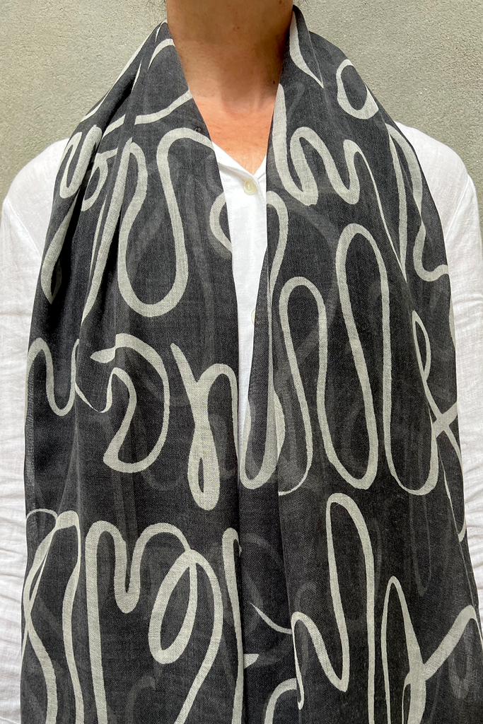 A woman wearing a soft and light weight See Design wool scarf with a black and white design.