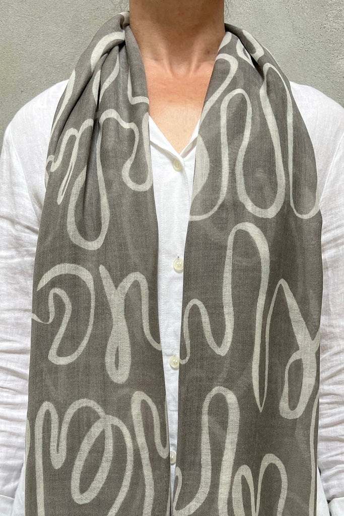 A woman wearing a See Design wool scarf with white writing on it.