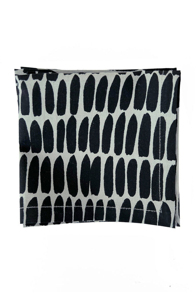 A folded cotton napkin from See Design's Cocktail Napkins (Set of 4) collection, featuring a black, oval-shaped pattern on a light background.