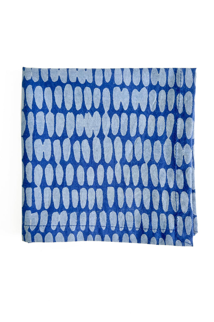 A set of four cocktail napkins by See Design, featuring a folded blue fabric with a pattern of white, elongated oval shapes—perfect for adding a colorful touch to your table linens.