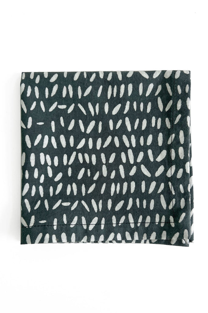 A black cotton cocktail napkin from the See Design set of 4, featuring an irregular white dot pattern, rests on a white background.