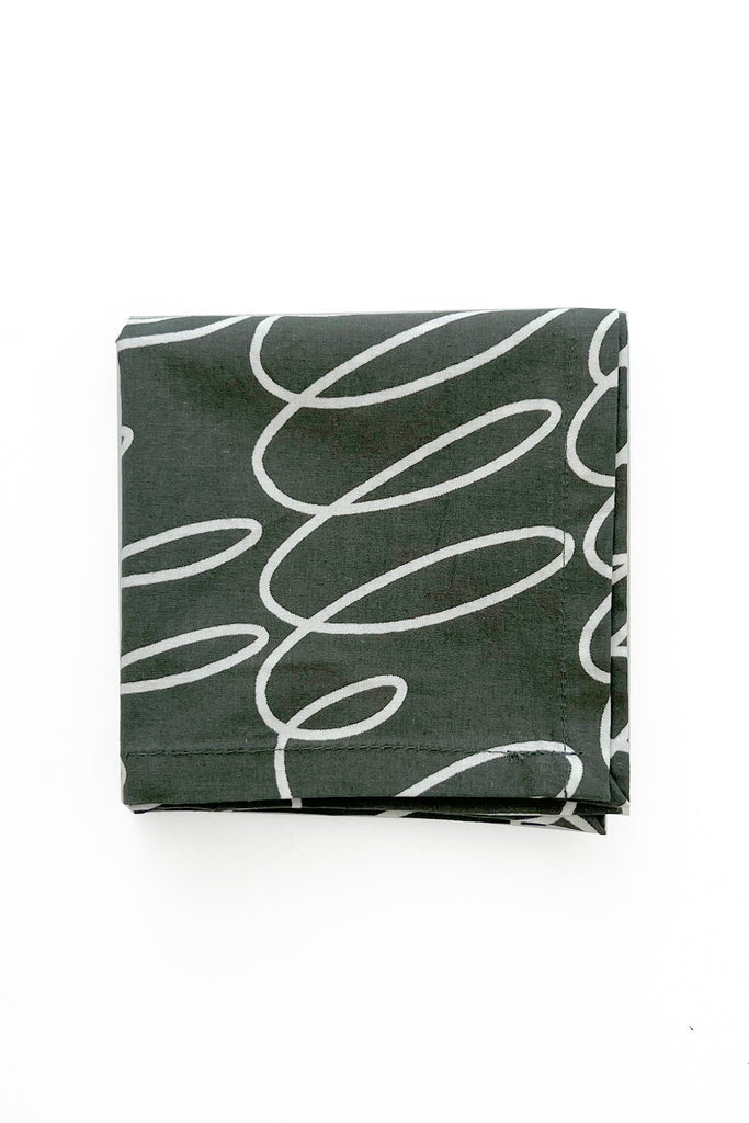 A folded napkin from See Design's Cocktail Napkins (Set of 4) in dark gray cotton, featuring a white abstract squiggle pattern, placed on a white background.