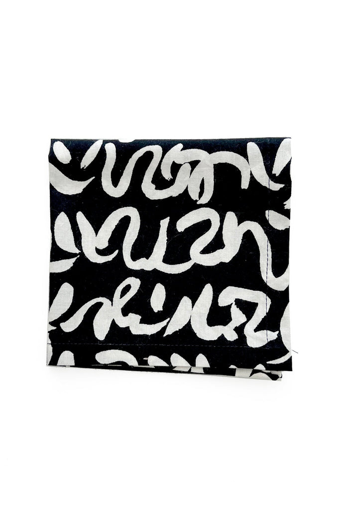 The Cocktail Napkins (Set of 4) by See Design feature a square piece of fabric with a black background and a white, abstract, wavy line pattern, making them the perfect complement to colorful table linens.