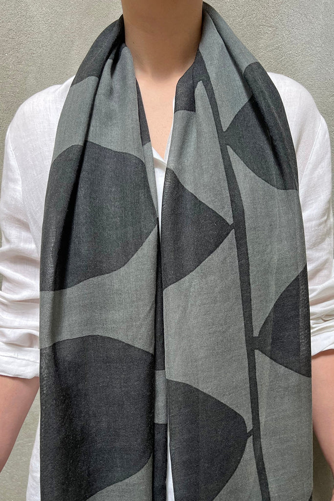 Person wearing a white shirt and a See Design Wool Scarf, which is black and gray patterned, hanging loosely around their neck.