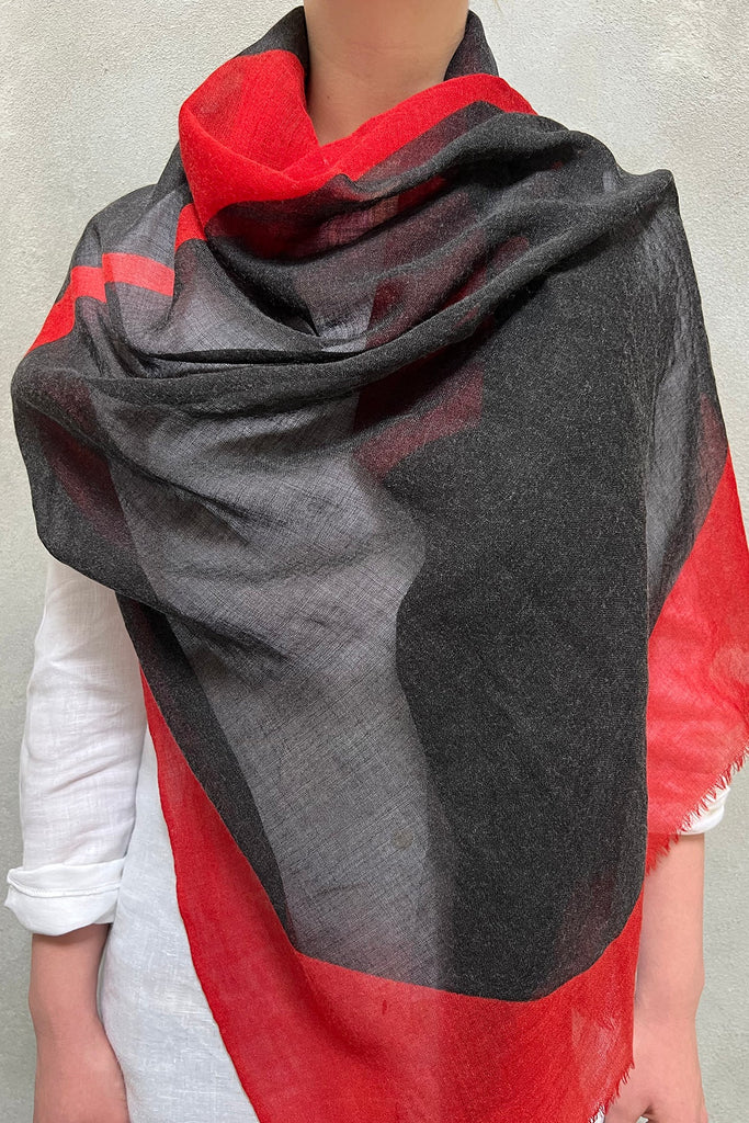 Person wearing a light gray shirt, with a See Design Wool Scarf in shades of red, black, and gray draped over their shoulders.