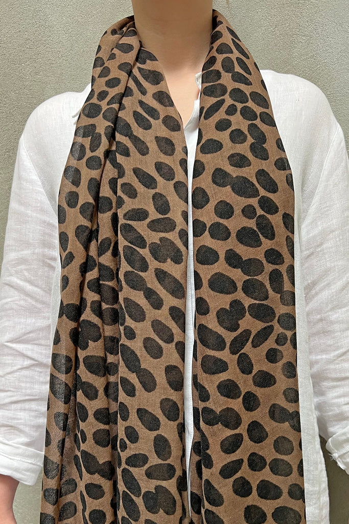 A person wearing a white shirt and a Wool Scarf by See Design featuring a black leopard print pattern, adding a touch of vibrant colors to their style.