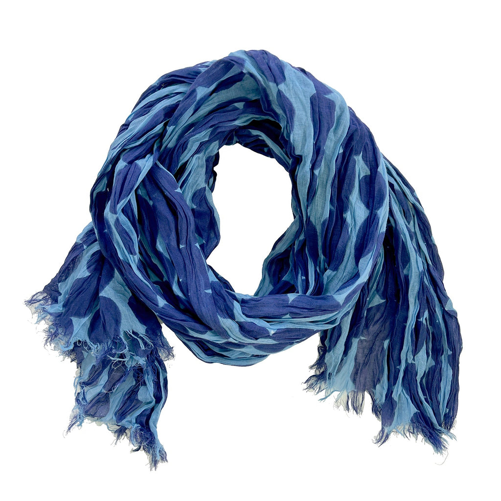 A crinkled, lightweight Cotton Scarf by See Design, featuring a pattern of varying blue shades and slightly frayed ends.
