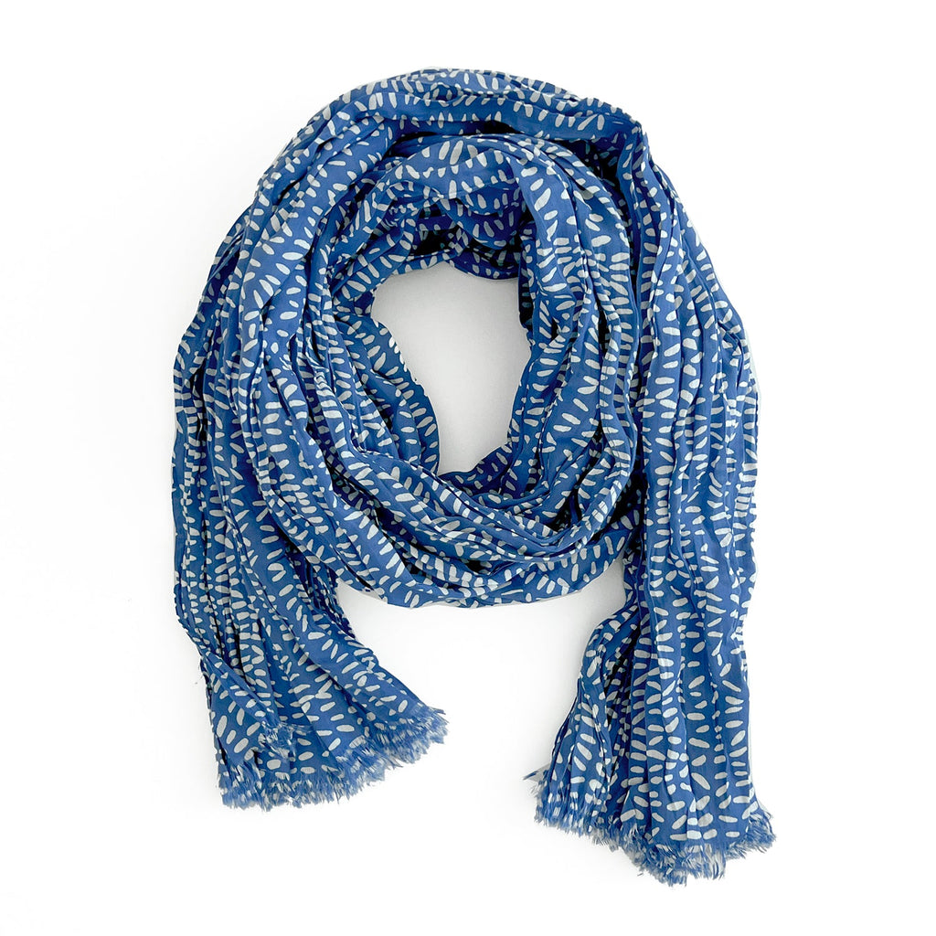 A blue Cotton Scarf by See Design, featuring a white leaf pattern, loosely coiled and made from soft, lightweight cotton, with fringe on the ends.