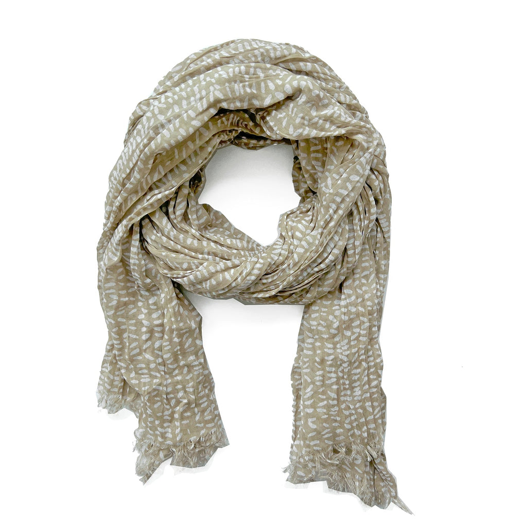 The See Design Cotton Scarf is a soft, lightweight accessory in light brown, featuring a white leaf pattern arranged in a semi-circle, with overlapping ends and frayed edges.