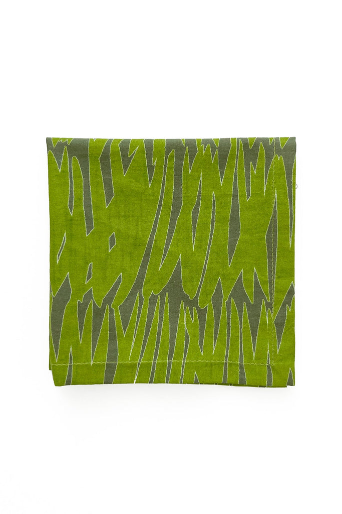 A folded piece of green fabric with an abstract, jagged pattern in a darker green shade resembles hand-painted designs. The See Design Cocktail Napkins (Set of 4) are displayed against a plain white background.