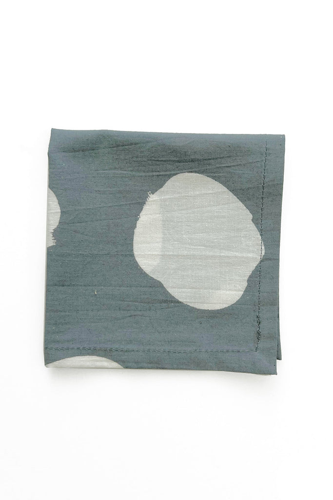 A folded piece of dark green fabric with large, irregular white circles, reminiscent of hand-painted designs, from the See Design Cocktail Napkins (Set of 4).