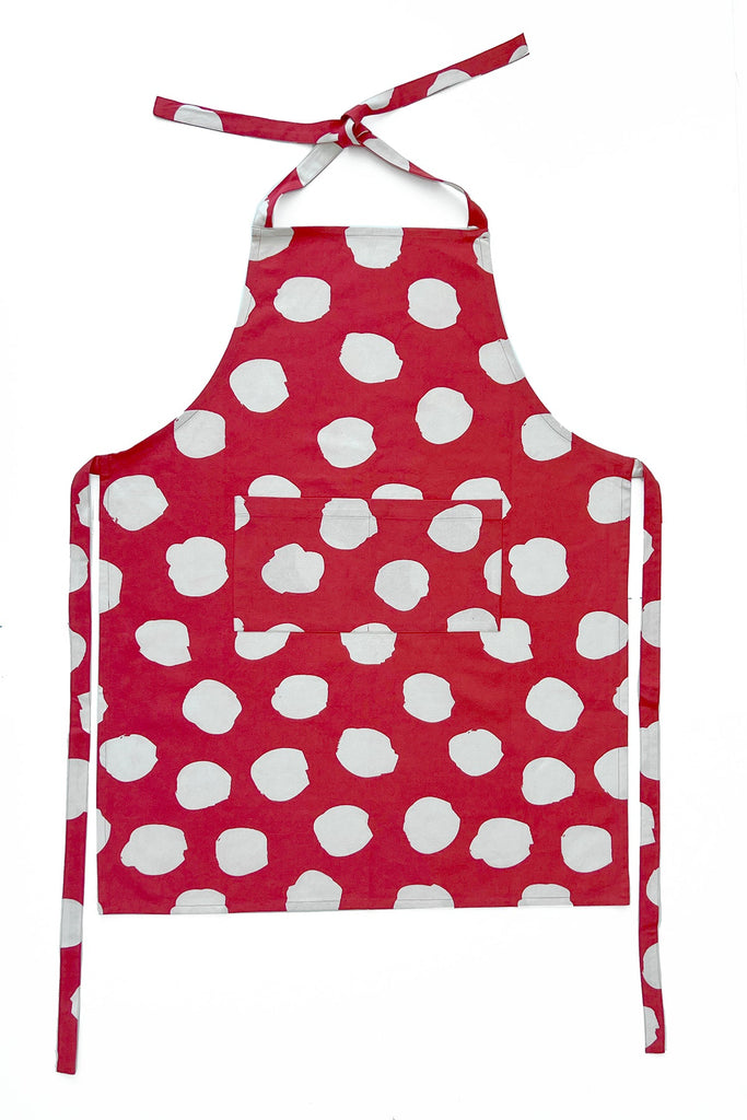 See Design Aprons: Red kitchen apron with white irregular polka dots, hand-painted design, front pocket, and adjustable neck and waist ties, shown on a white background.