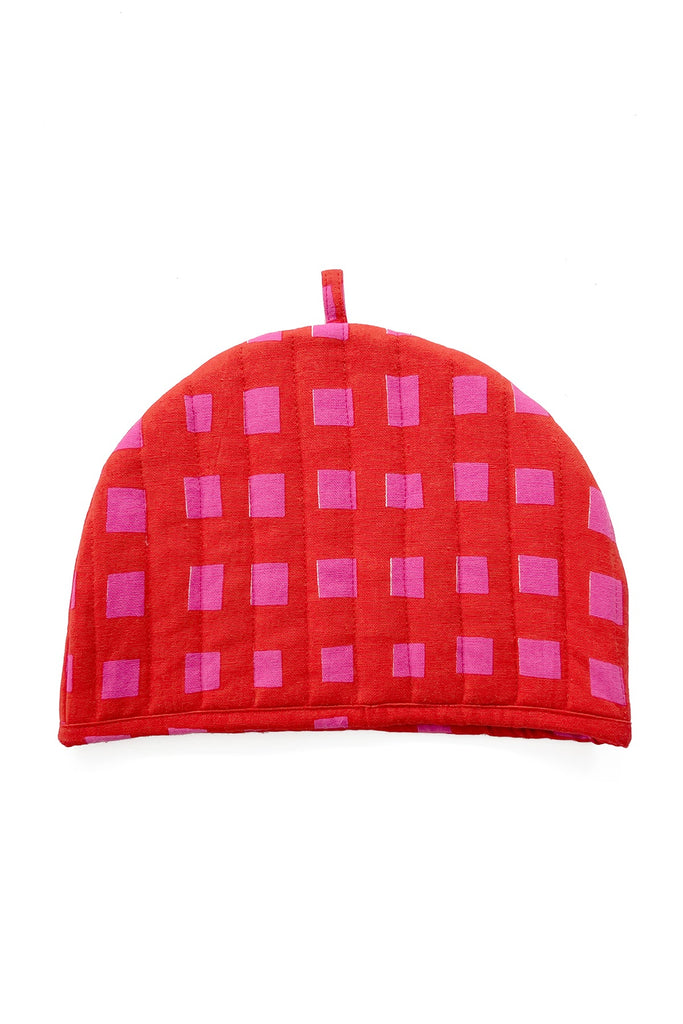 The See Design Tea Cosy, with a red and pink checkered pattern, semicircular shape, and top loop, is featured in our fall home collection and displayed on a white background.