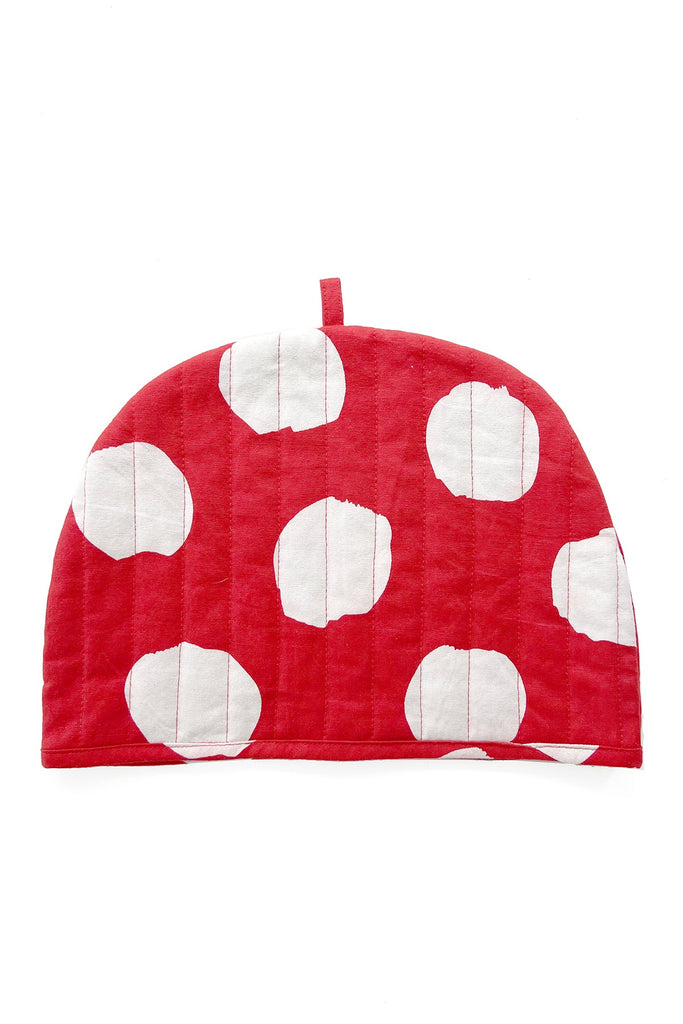 The See Design Tea Cosy features large, irregular white polka dots on red fabric, a small top loop, and hand-painted details, shown against a white background.