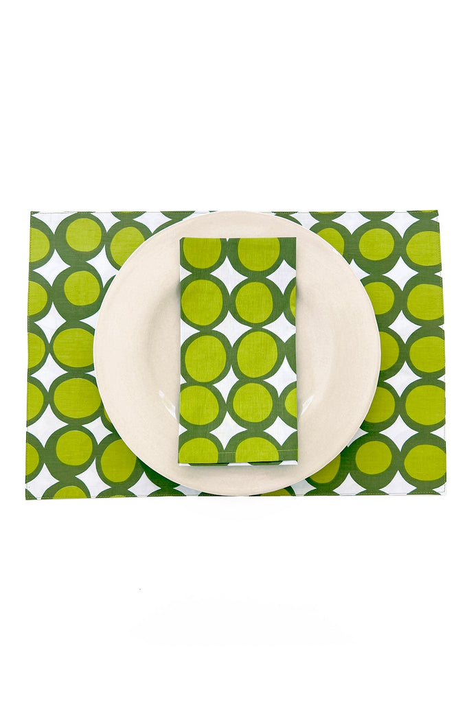 A white plate with a green patterned napkin sits atop See Design’s Placemats (Set of 2), coordinated with the green and white table linens underneath.
