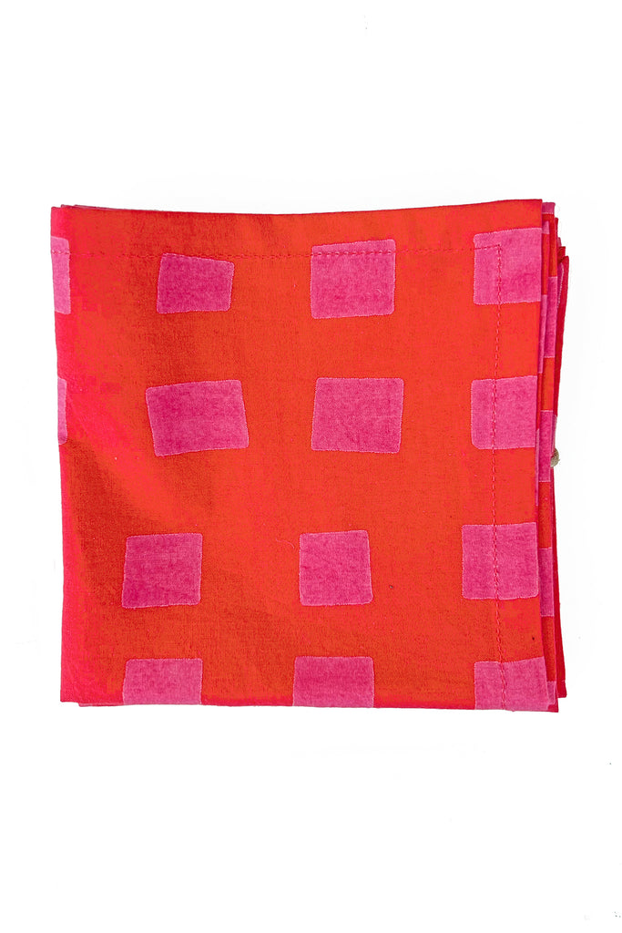 See Design’s Cocktail Napkins (Set of 4) feature a folded rectangular cotton design with a red background and pink rectangular patterns, displayed on a white surface—perfect for adding elegance to colorful table settings.
