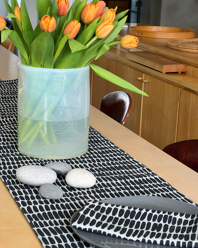 A black and white See Design cotton table runner with tulips in a vase.