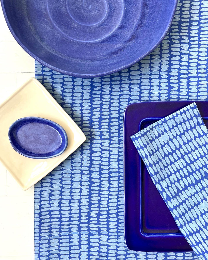 A blue See Design table runner with a napkin set on a table.