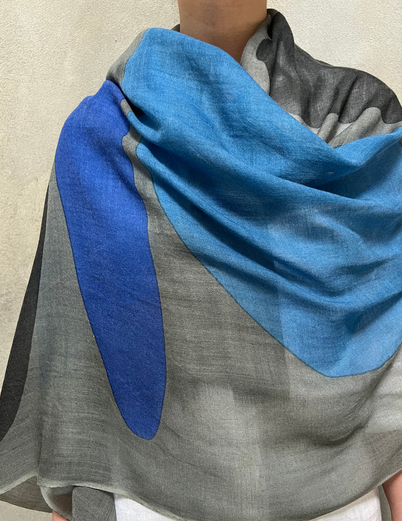 Person wearing a See Design wool scarf featuring stunning abstract patterns in blue, grey, and black.
