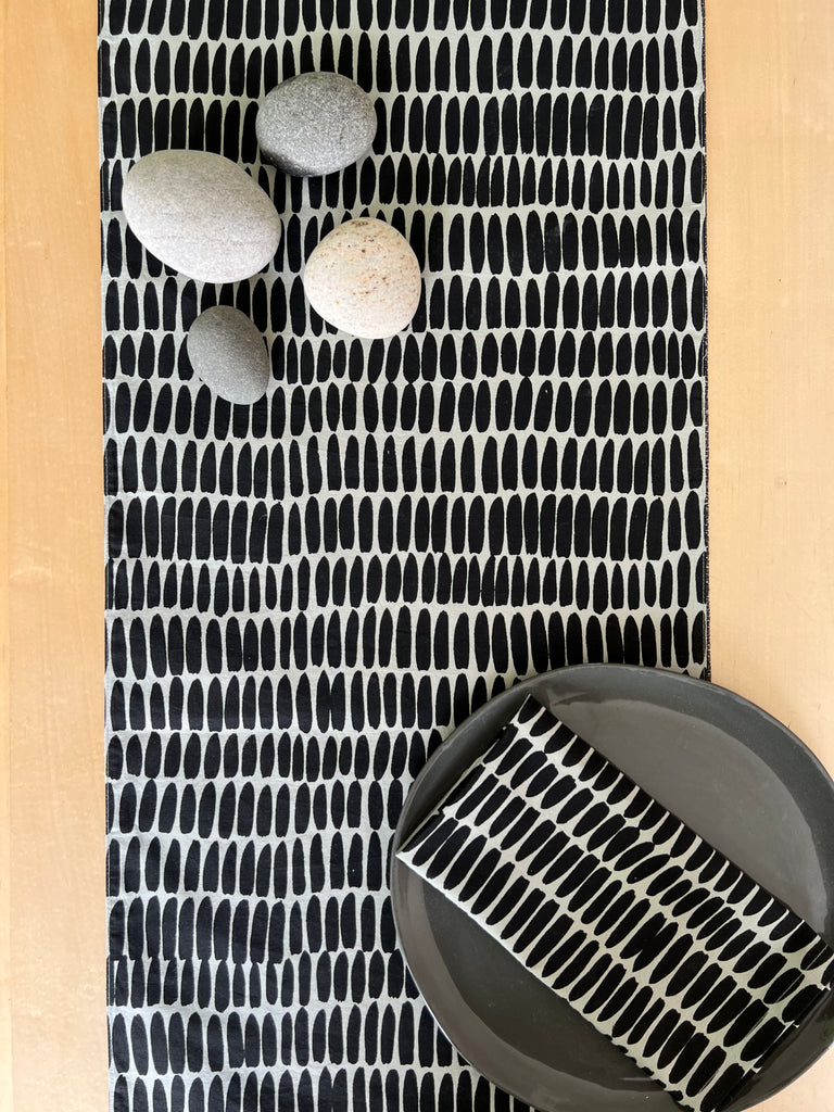 A See Design cotton table runner with black and white prints on a wooden table.