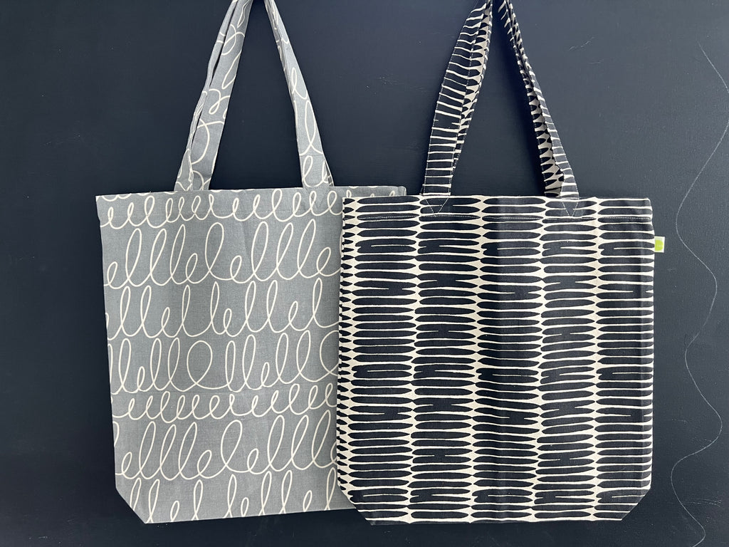 Two lightweight, cotton canvas Easy Tote bags with hand-painted artwork on a black background by See Design.