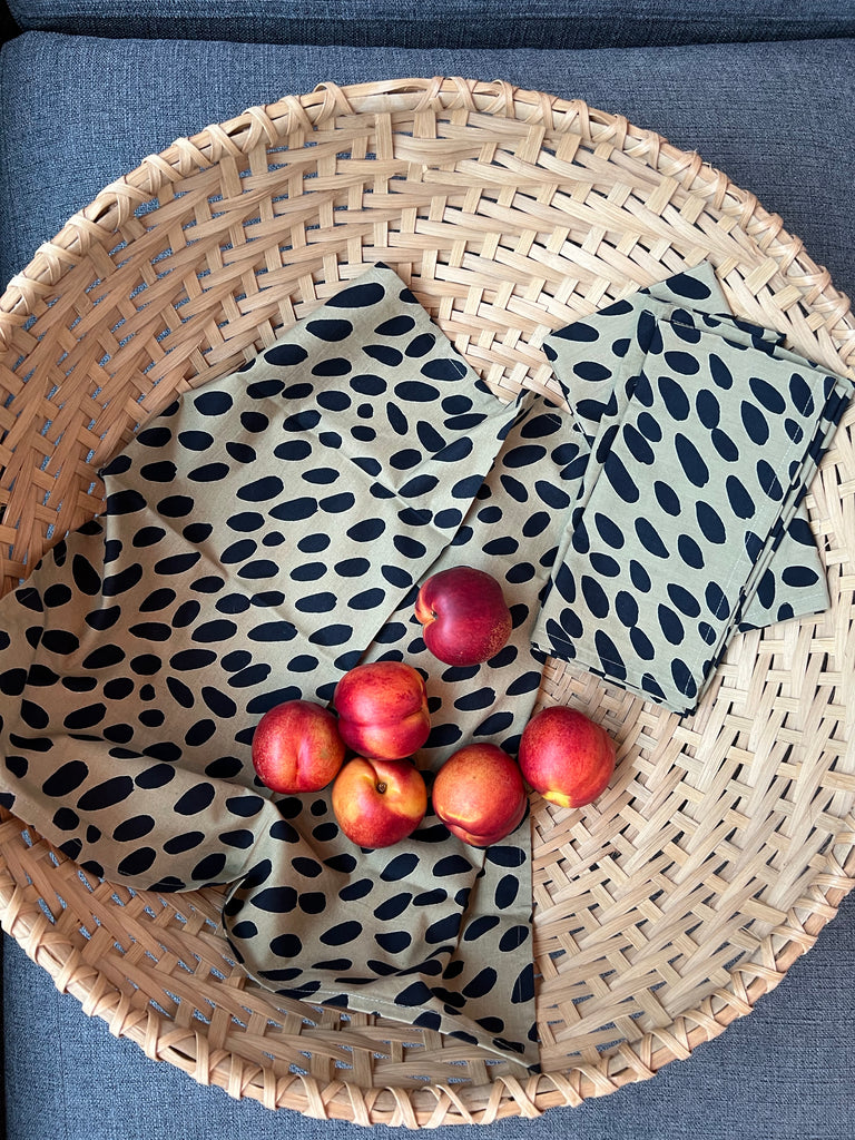 A wicker basket filled with fruit and vibrant See Design cotton napkins (Set of 4).