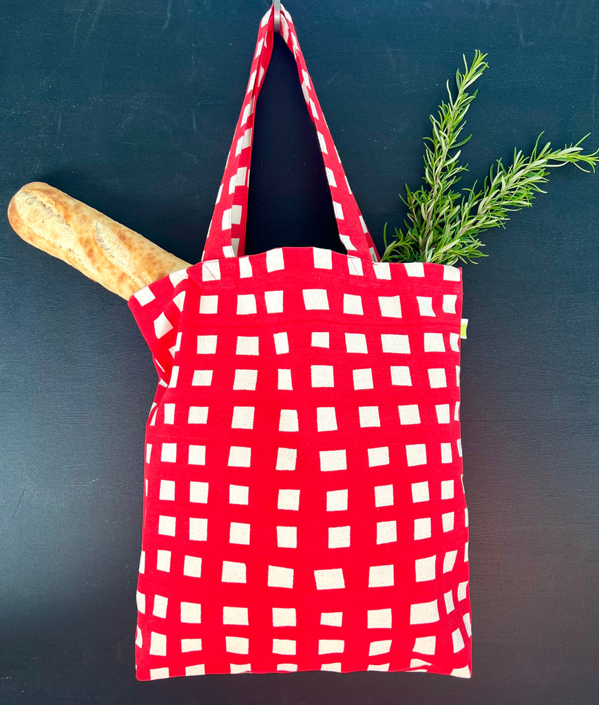 A lightweight, red and white gingham cotton canvas Easy Tote Bag with hand-painted artwork by See Design and a wooden spoon.