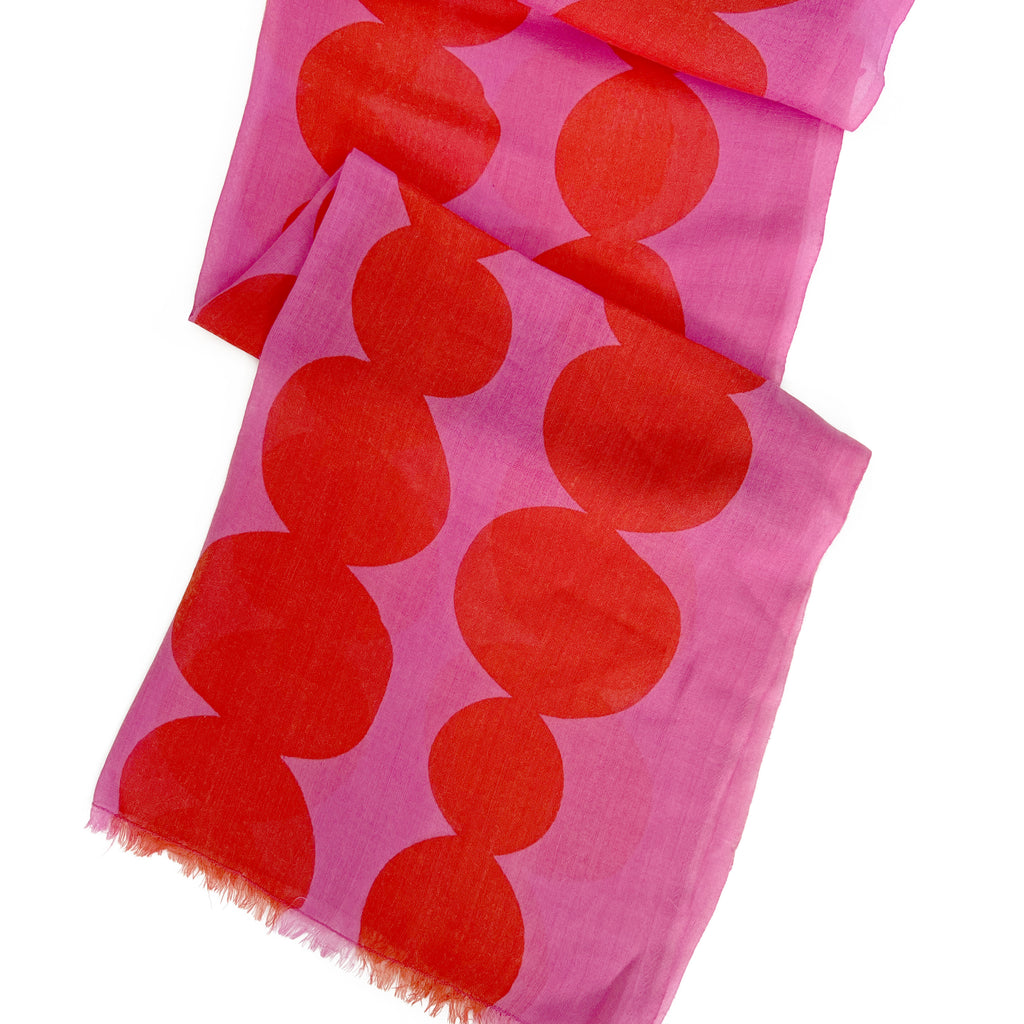 A pink wool scarf from See Design, featuring a repeating pattern of large red circles and slightly frayed ends.