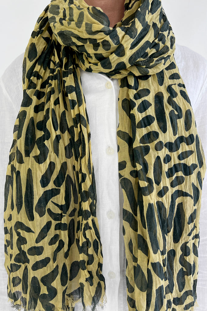A woman wearing a vibrant yellow and black leopard print Cotton Scarf by See Design.