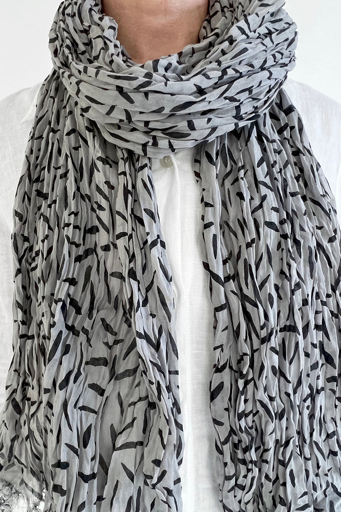 A woman wearing a lightweight See Design cotton scarf with black and white leaves on it.