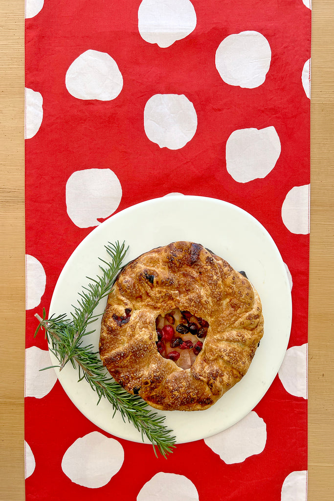 A rustic fruit galette on a white plate sits atop the See Design Table Runner, featuring bold white polka dots for a charming table setting.