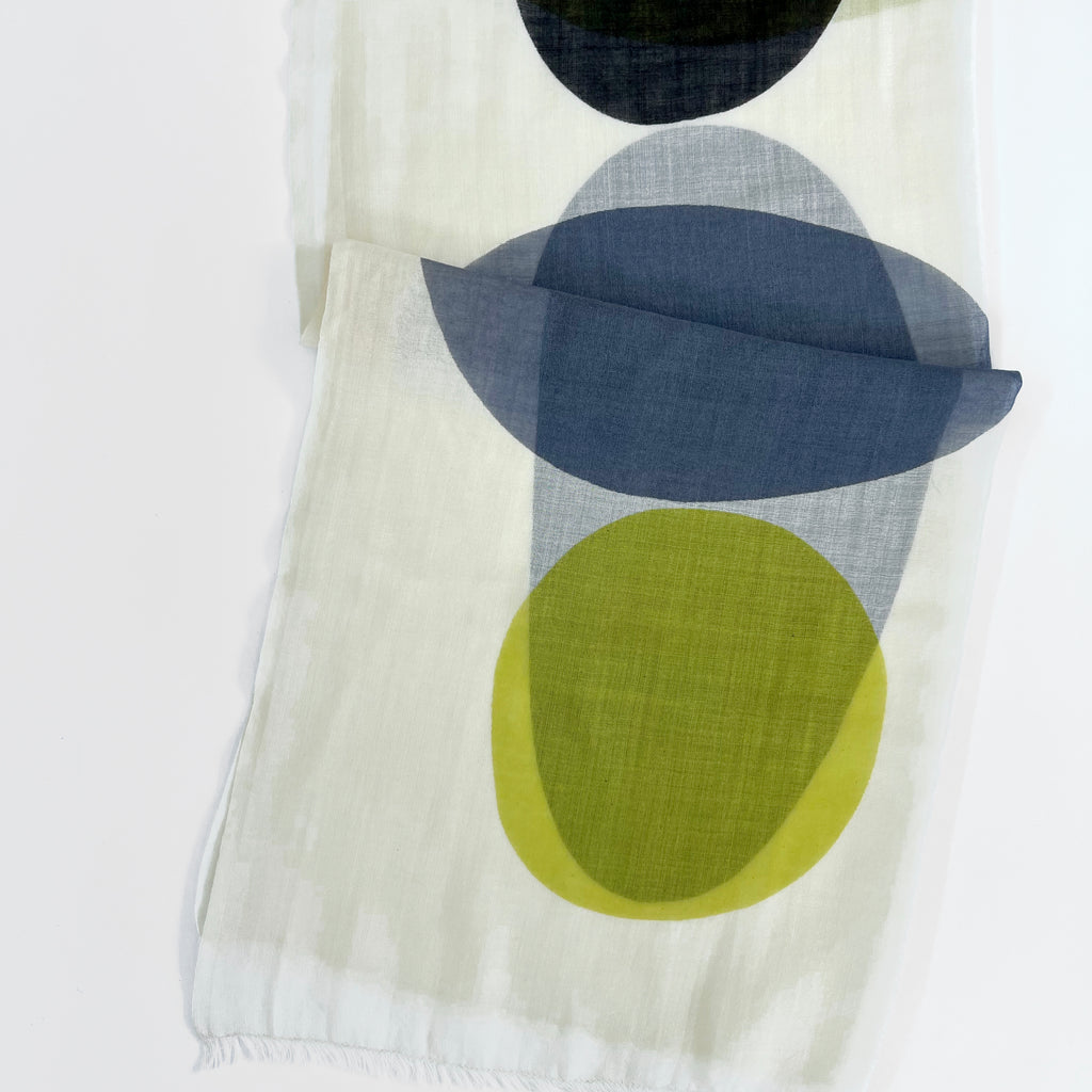 The Wool Scarf by See Design features Donna Gorman’s white fabric with vertically arranged overlapping ovals in black, gray, blue, and yellow-green—a minimalist, lightweight accessory.