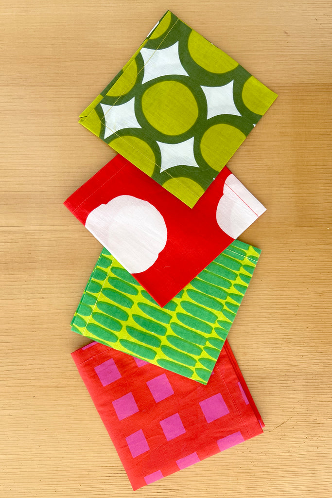 The See Design Cocktail Napkins (Set of 4) feature bold, colorful geometric patterns and are arranged on a wooden surface—perfect for adding vibrant flair to your colorful table linens collection.