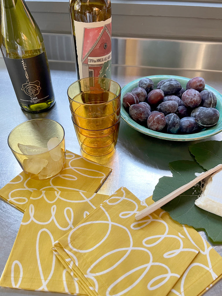 A bottle of wine and grapes on a table with See Design Cocktail Napkins (Set of 4).