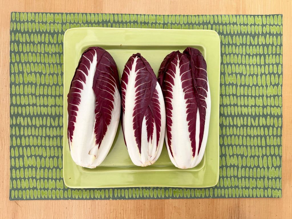 Three endives with purple and white leaves arranged on a green rectangular plate placed on a See Design patterned green cotton placemat from the Placemats (Set of 2), enhancing the dining experience.