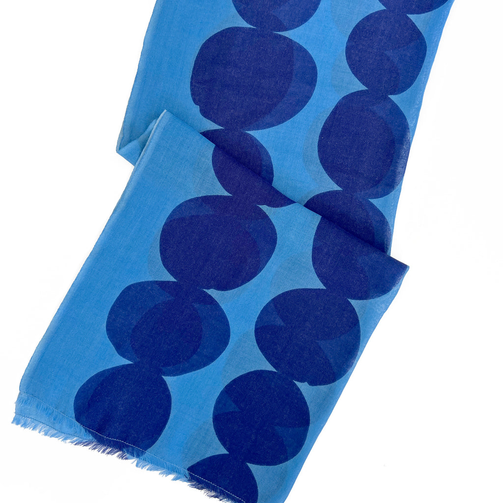 The See Design Wool Scarf is a blue lightweight shawl with large dark blue circles on a lighter blue background and unfinished fringed edges, perfect for adding style to your collection. Designed by Donna Gorman.
