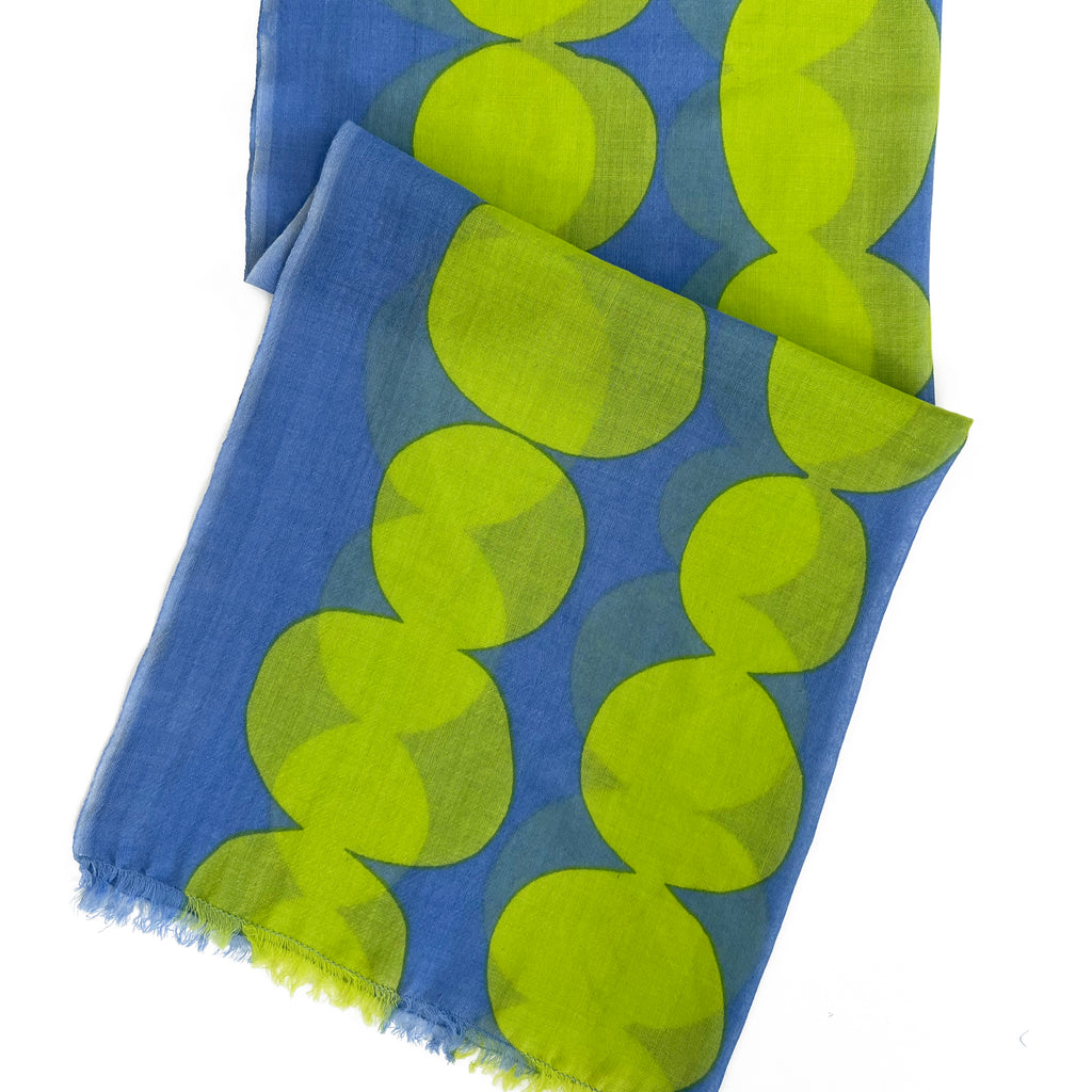 A lightweight wool scarf by See Design, this blue accessory features large overlapping bright green circles and a slightly frayed edge—a modern update on the classic shawl.