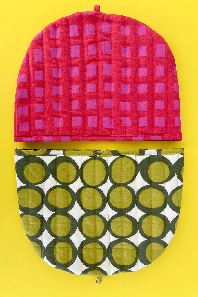 Two semi-circular See Design Tea Cosies from the fall collection are shown on a yellow background: the top is red with a square pattern, and the bottom is green with a circular pattern.